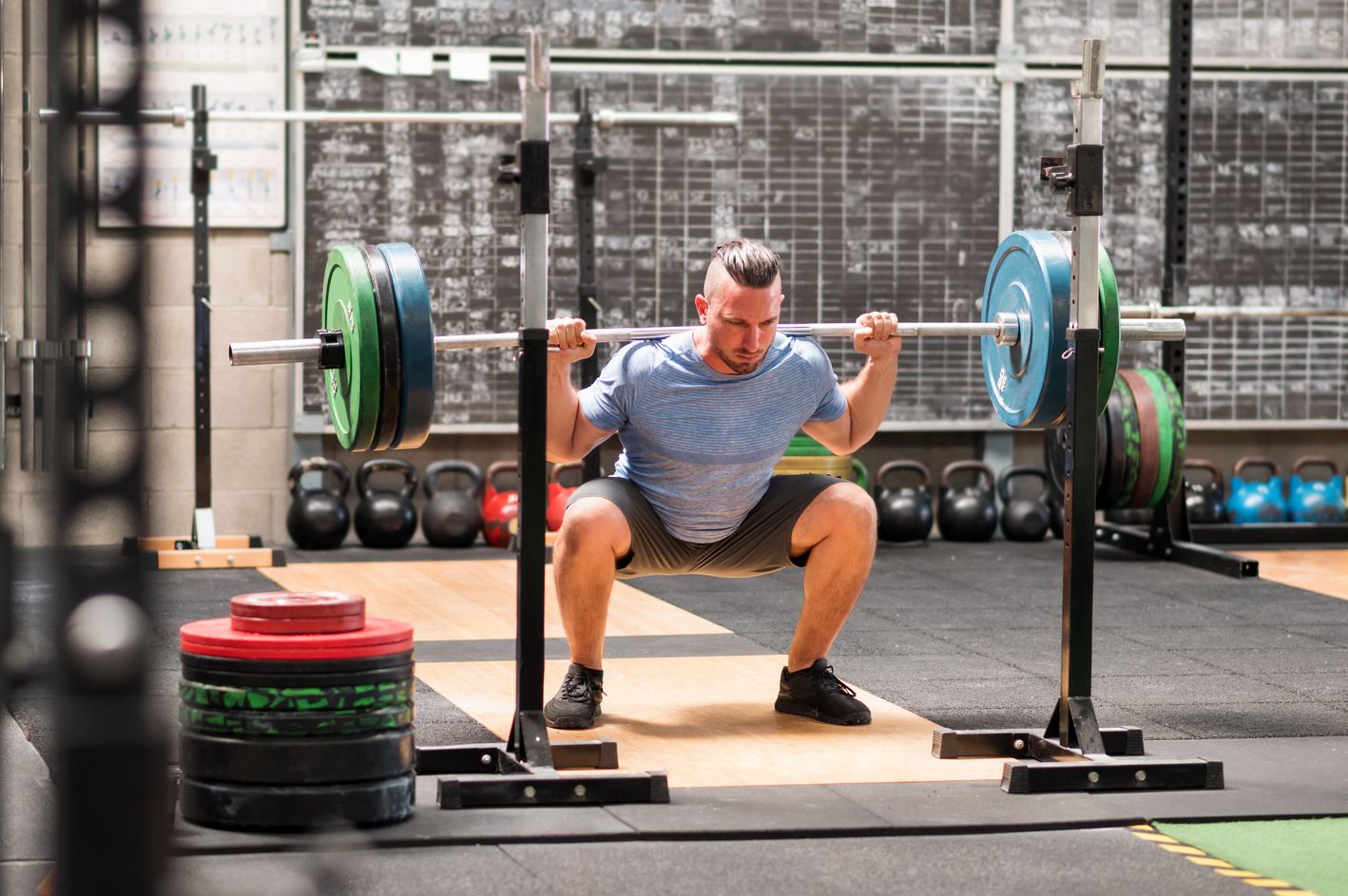 Sportsman doing back squat exercise with barbell in gym